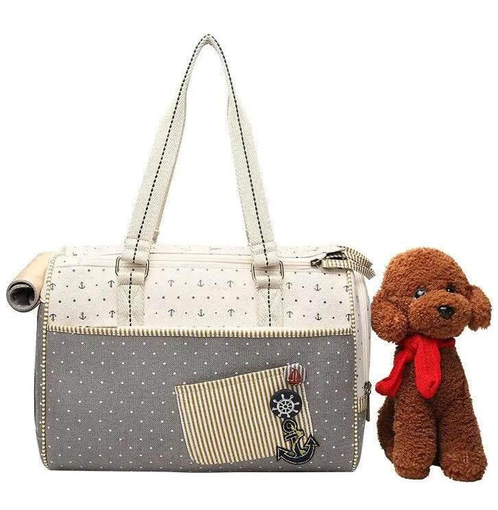 Nautical-style pet carrier bag with anchor patch, beside fluffy brown dog wearing red scarf