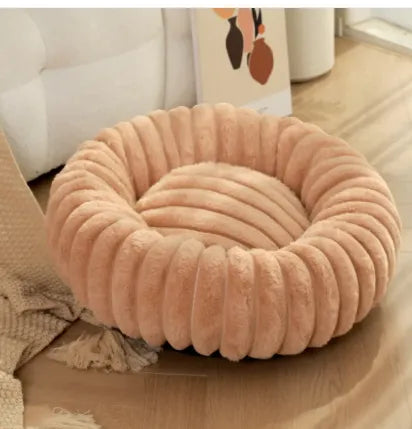 Round plush pet bed in a soft peach color on a wooden floor.