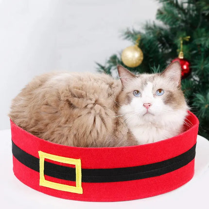 Fluffy ragdoll cat resting in a red felt Santa-style holiday bed with a Christmas tree background.