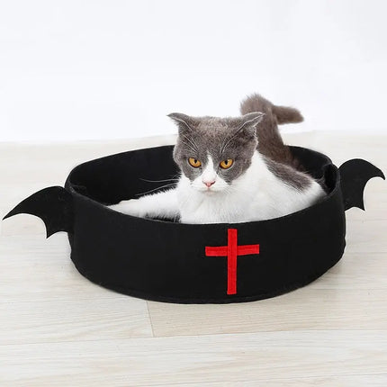 Grey and white cat resting in a black felt holiday bed with a red cross design.
