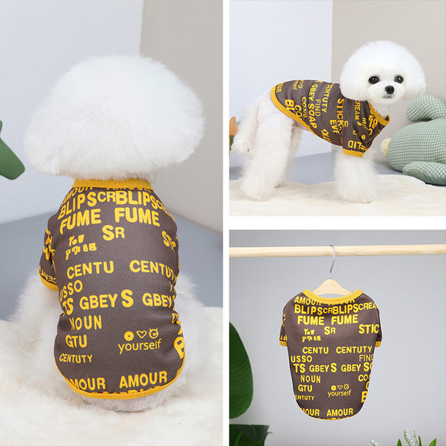 Small white dog wearing a brown graphic print pet t-shirt with yellow lettering.
