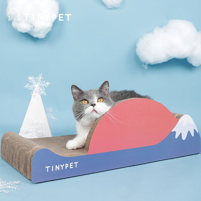 Gray and white cat lounging on colorful TINYPET cardboard scratcher with mountain design, perfect for pet care and play.